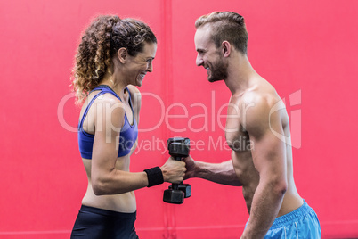 Laughing muscular couple lifting dumbbells