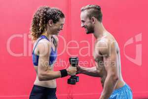 Laughing muscular couple lifting dumbbells