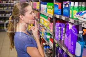 Thoughtful pretty brunette looking at product in shelf