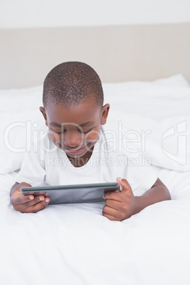 Pretty smiling little boy using digital tablet in bed