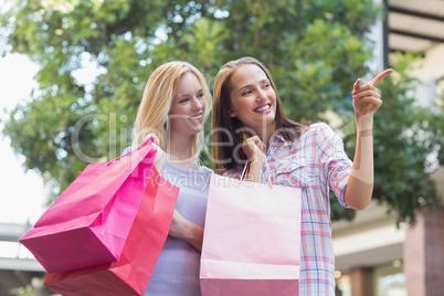 Happy women with shopping bags and pointing away