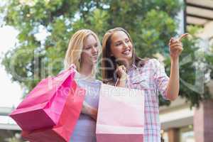 Happy women with shopping bags and pointing away