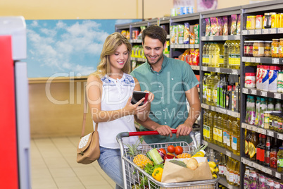 Smiling bright couple buying food products and using notebook