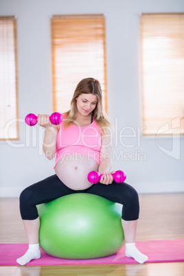 Pregnant woman lifting dumbbells on exercise ball