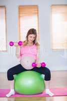 Pregnant woman lifting dumbbells on exercise ball