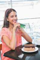 Young happy woman holding credit card and a cake in front of her