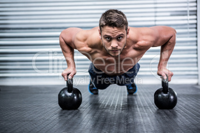 Portrait of muscular man doing push-ups with kettlebells