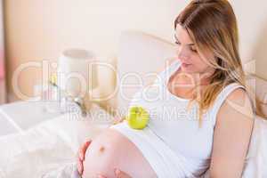 Pregnant woman lying on bed with apple in belly