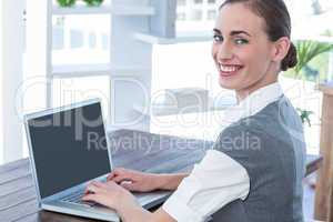 Businesswoman looking at camera and using laptop