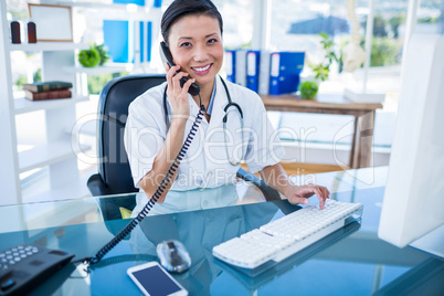 Smiling doctor having phone call and using her computer