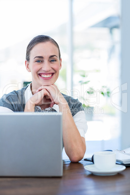 Happy businesswoman looking at camera behind laptop computer