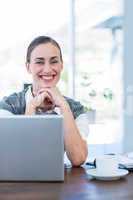 Happy businesswoman looking at camera behind laptop computer