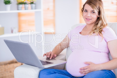 Pregnant woman looking at camera and using laptop