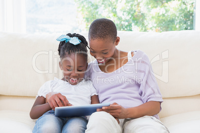 Happy smiling mother using tablet with her daughter on couch