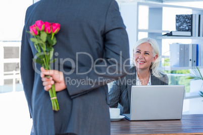 Businessman hiding flowers behind back for colleague