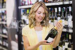 Smiling pretty blonde woman looking at wine bottle