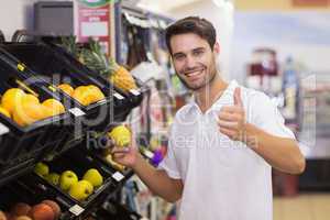 Portrait of a smiling handsome man buying a fruit with thumb up