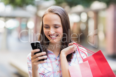 Pretty brunette using her smartphone and holding shopping bag