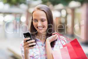 Pretty brunette using her smartphone and holding shopping bag