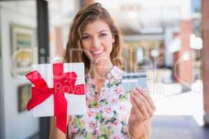 Portrait of smiling woman showing gift box and credit card to th