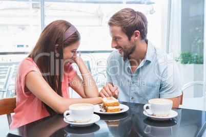 Young happy couple looking at each other while eating cake