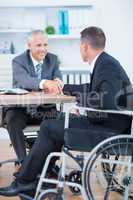 Businessman in wheelchair shaking hands with colleague
