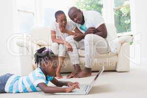 Pretty couple sitting on couch and their daughter using laptop