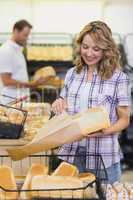 Smiling blonde woman taking a bread in her paper bag