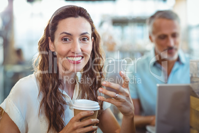 Pretty brunette looking at camera with smartphone and coffee in
