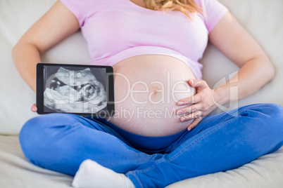 Pregnant woman showing ultrasound scans and touching her belly