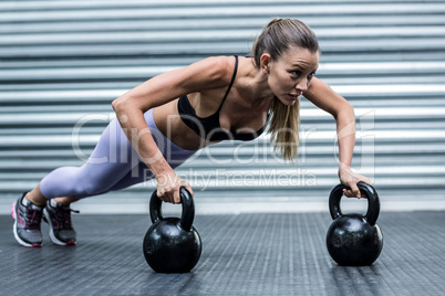 Muscular woman doing pushups with kettlebells