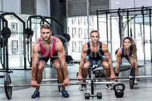 Three muscular athletes lifting a barbell