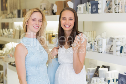 Happy women smiling at camera and holding bottle of perfume