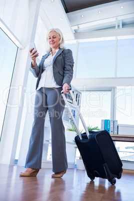 Businesswoman using smartphone and holding suitcase