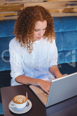 Pretty ginger having coffee using laptop