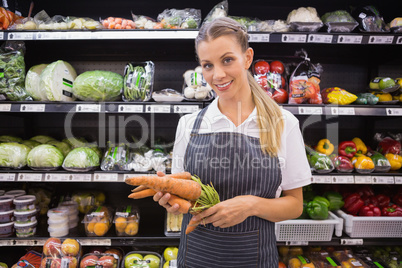 Pretty blonde woman holding carrot and looking at camera