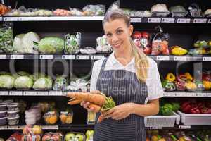 Pretty blonde woman holding carrot and looking at camera