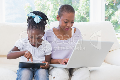 Happy smiling mother using laptop with her daughter using tablet