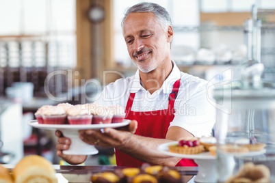 Happy barista holding a plate of cupcakes