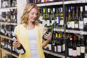 Smiling pretty blonde woman looking at wine bottle