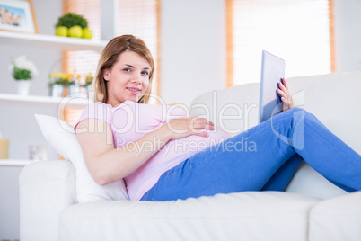 Pregnant woman looking at camera and using tablet