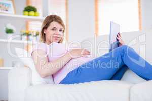 Pregnant woman looking at camera and using tablet