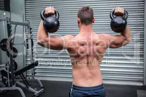 Muscular man lifting two kettlebells