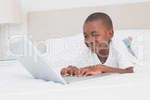 Pretty little boy using laptop in bed
