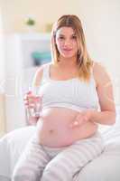 Pregnant woman sitting on bed  and holding glass of water