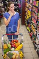 Thoughtful pretty woman pushing trolley in aisle