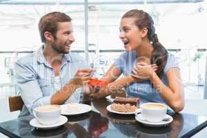 Young happy couple eating cake and man giving her a ring