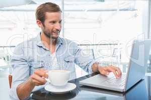 Young happy man typing on the laptop while holding his coffee