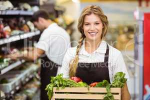 Portrait of smiling staff woman holding a box with fresh vegetab