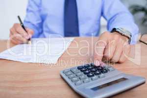 Businessman using the calculator while writing